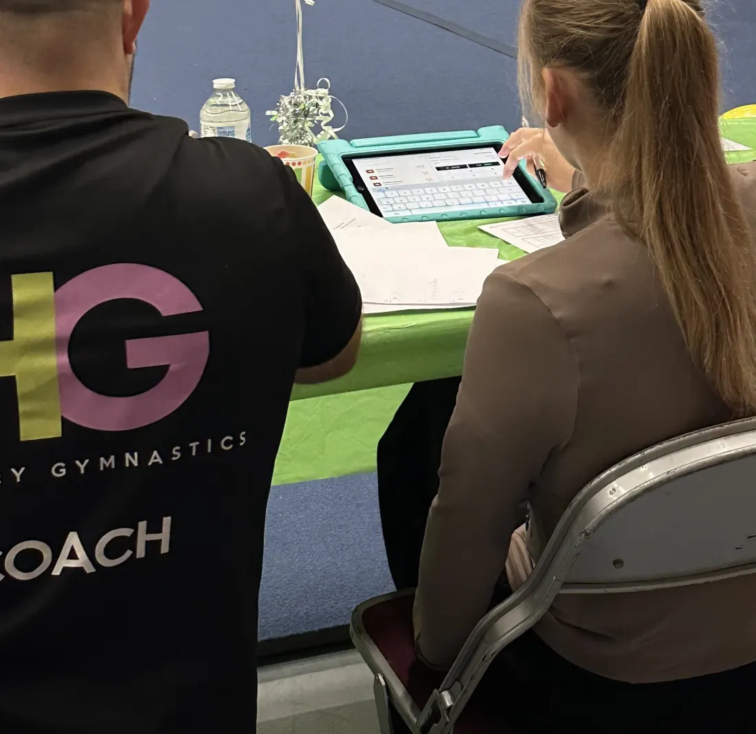 Two Hockley Gymnastics Club coaches, seen from behind, entering scores on an iPad at the judges' table